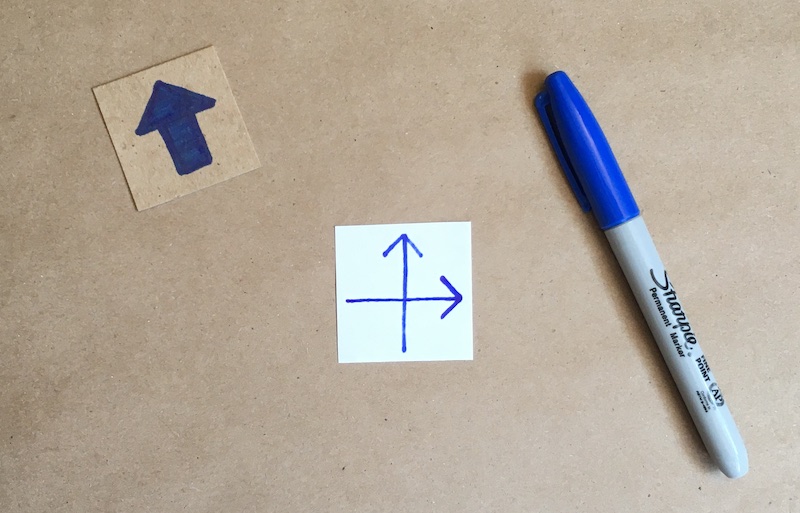 An arrow showing through a square of paper, with another arrow drawn on the front