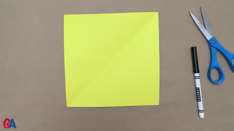 Square of yellow paper with scissors